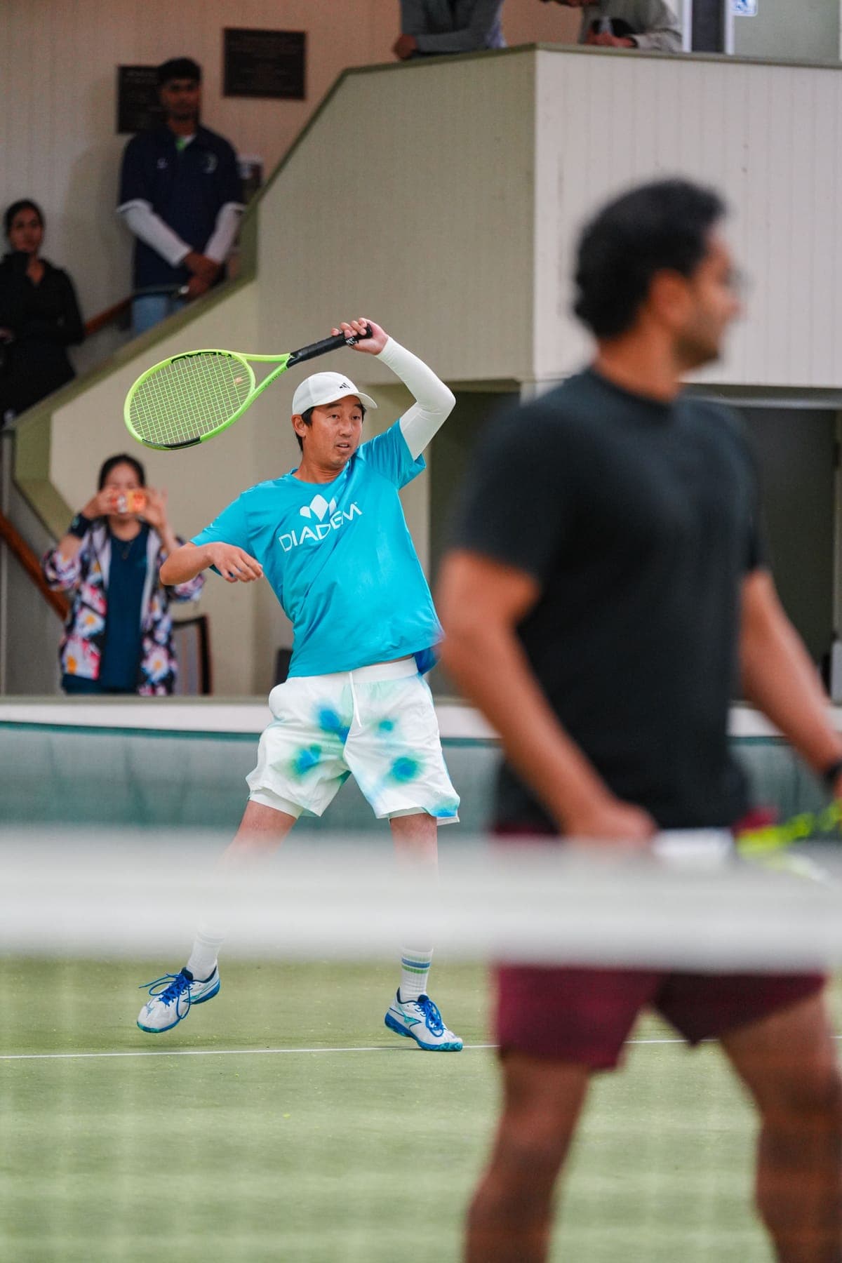 A challenger in a Diadem shirt winding up a forehand