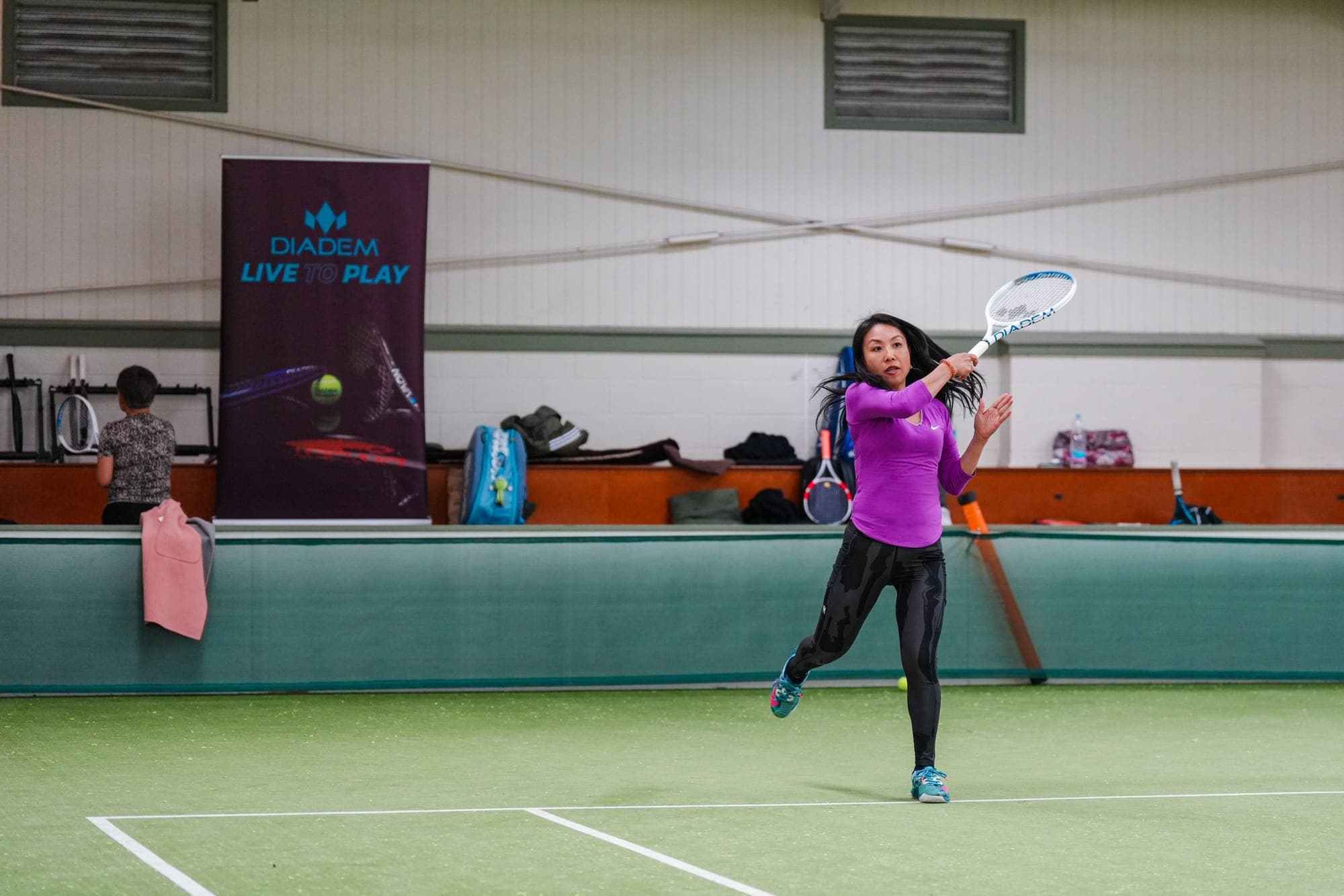 A player hitting a forehand in front of a Diadem Live to Play banner